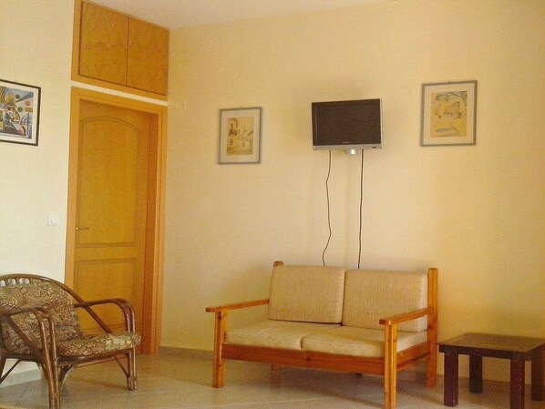 A living room with a wooden chair, a sofa, a small table, and a TV mounted on the wall. - Apartment in Ravdoucha with Sea Views (Voukolies)