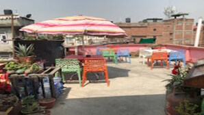 Une terrasse sur le toit avec des chaises colorées, un grand parasol à rayures et des plantes en pot.