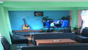 Un salon avec une télévision, une guitare, ainsi que plusieurs chaises et tables.
