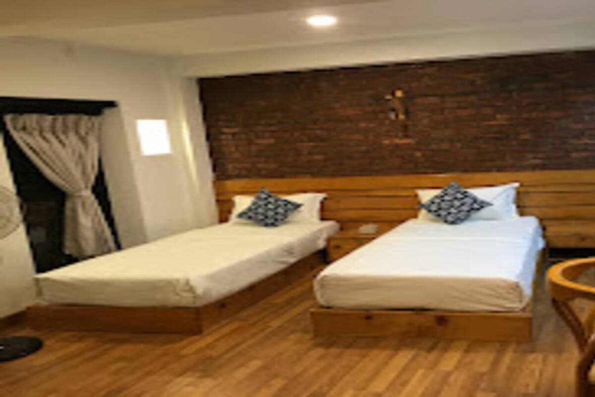 Une chambre avec deux lits simples, des têtes de lit en bois, une petite table en bois et un mur en briques.