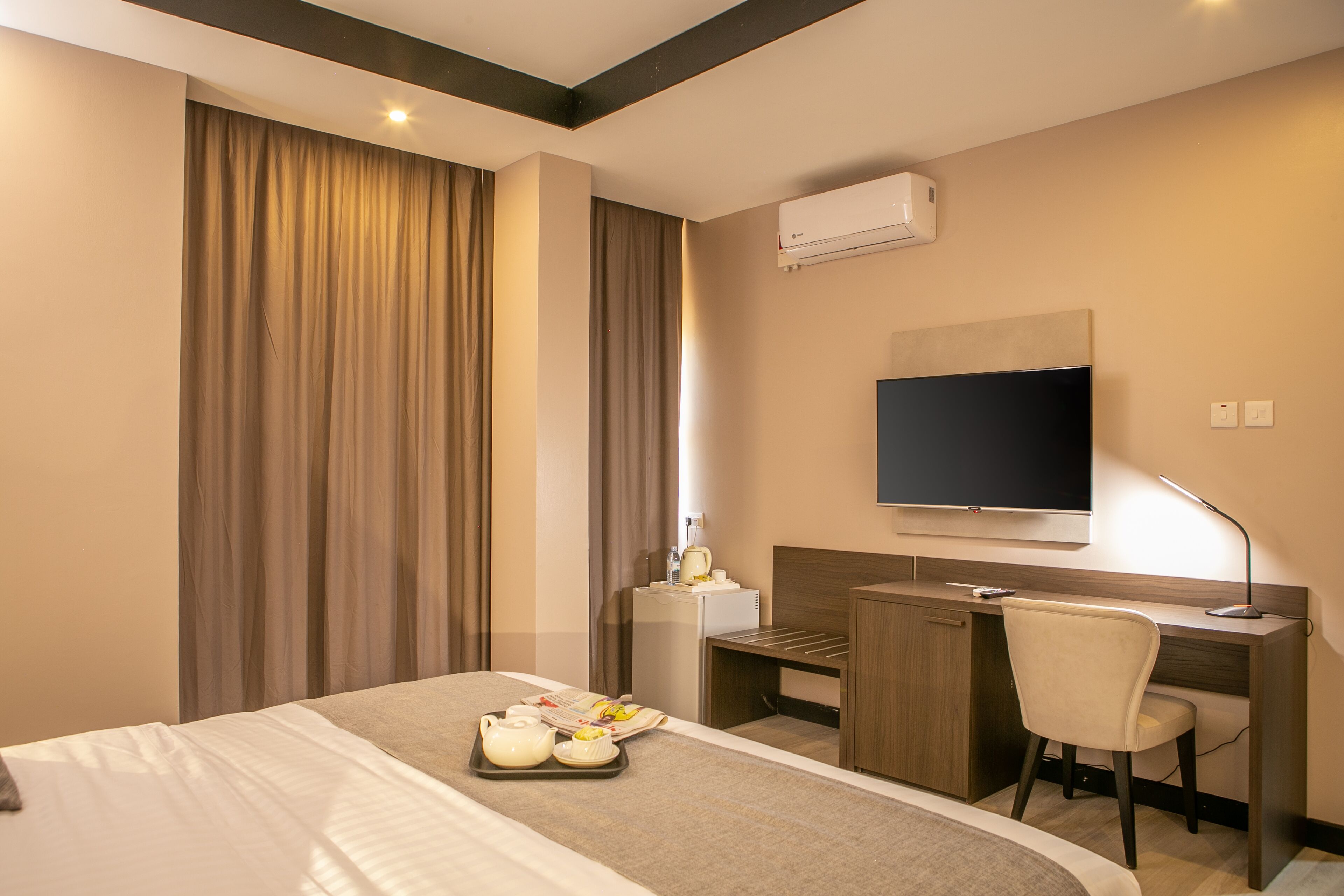 A hotel room with a bed, a desk, a chair, a television, and a tray with breakfast items.