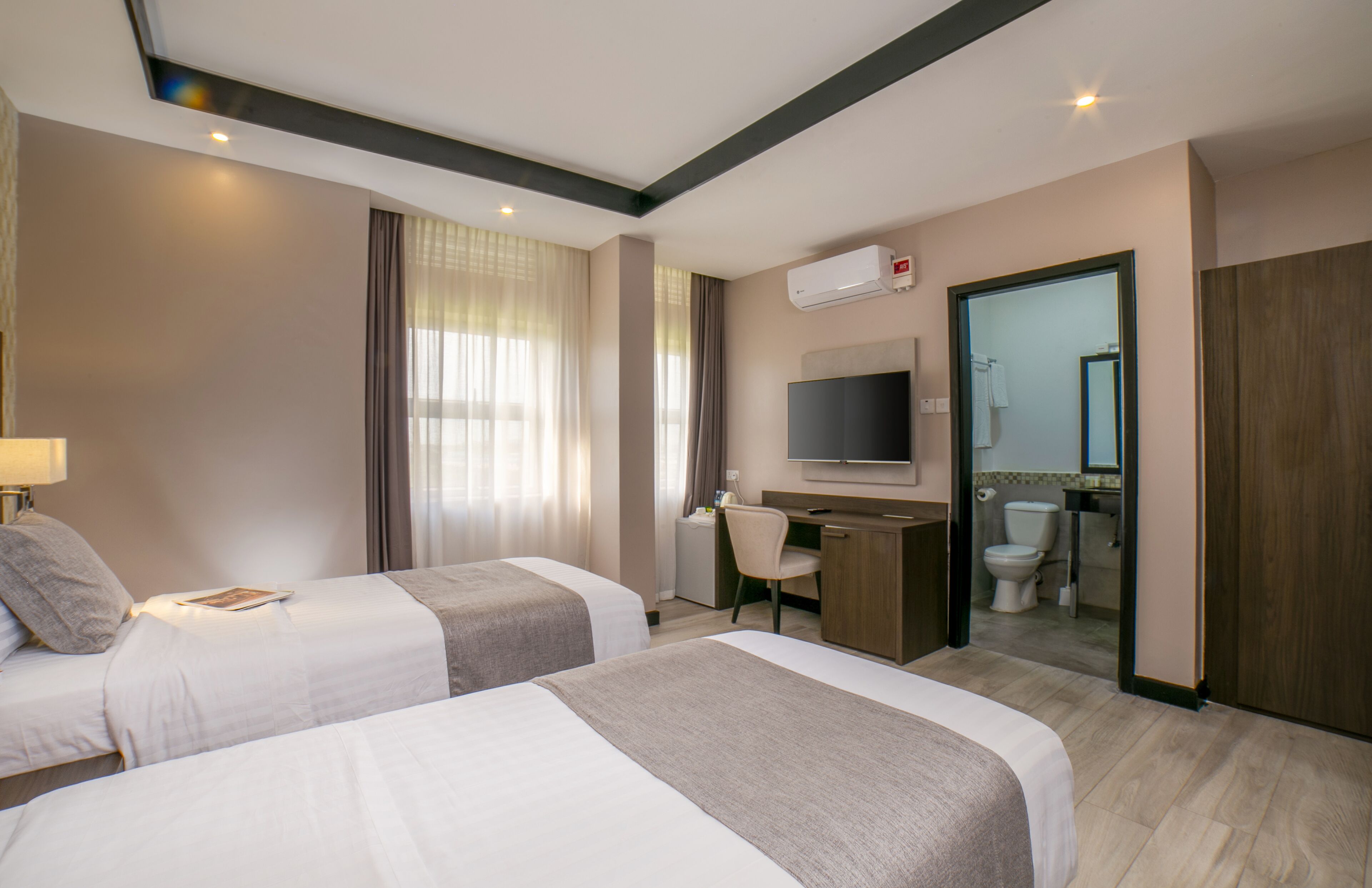 A hotel room with two beds, a desk, a TV, and a bathroom visible through an open door.