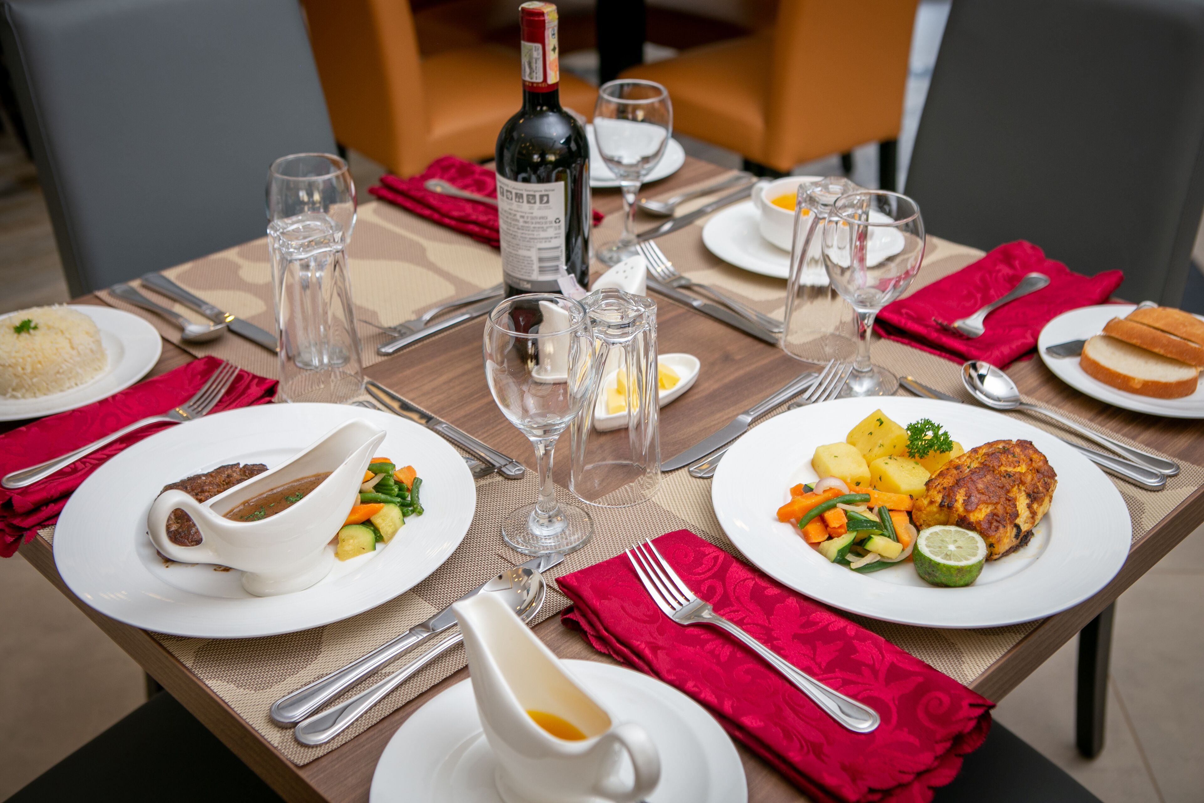 Una mesa de comedor dispuesta con platos de comida, vasos y cubiertos.
