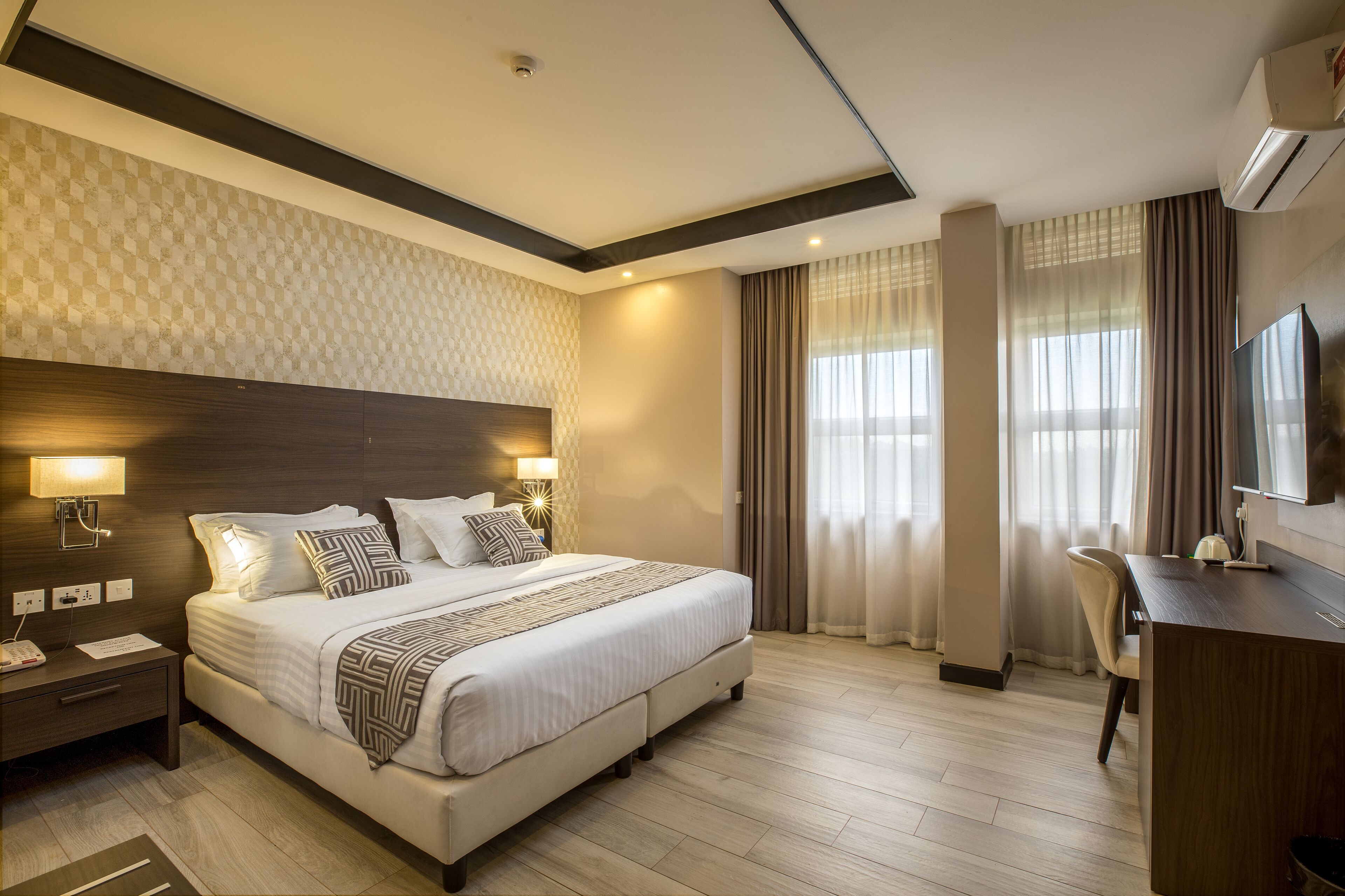 Quarto de hotel moderno com uma cama grande, abajures, uma escrivaninha e uma televisão.