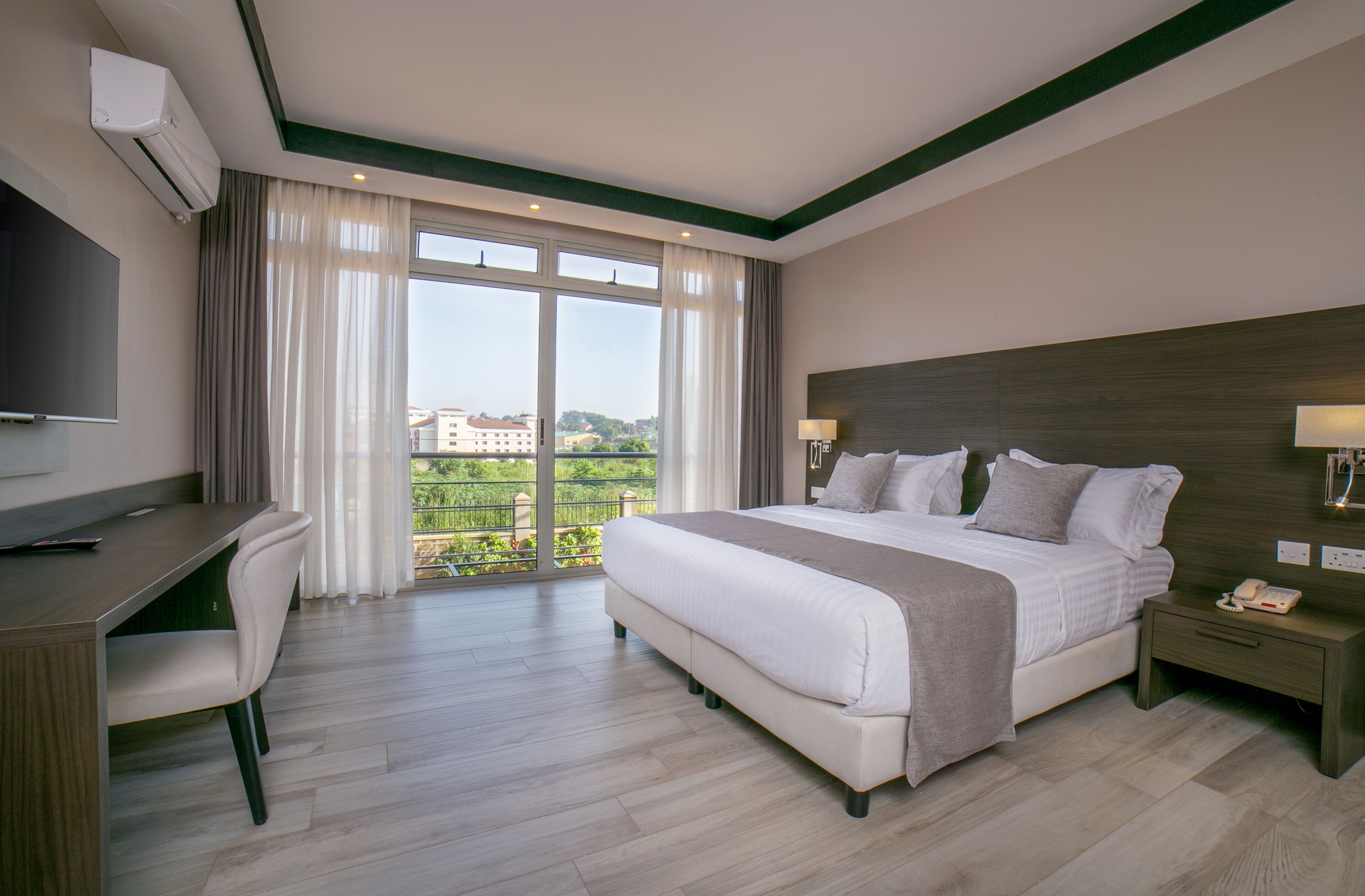 Ein Hotelzimmer mit einem großen Bett, einem Schreibtisch, einem Sessel, einem Fernseher und Blick auf die Stadt.