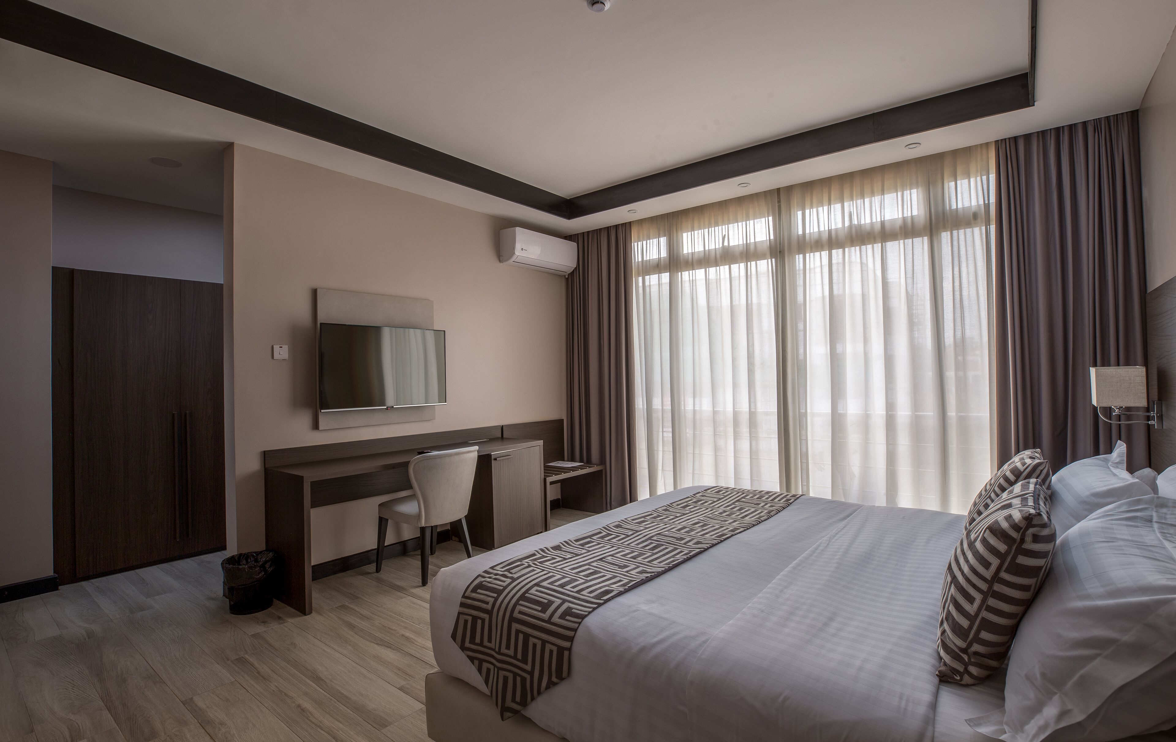 Habitación de hotel con una cama grande, un escritorio con silla, televisor de pantalla plana y un ventanal con cortinas.