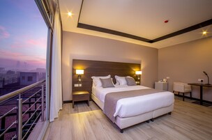 Una habitación de hotel moderna con una cama grande, lámparas de noche, un escritorio y vistas a la ciudad.