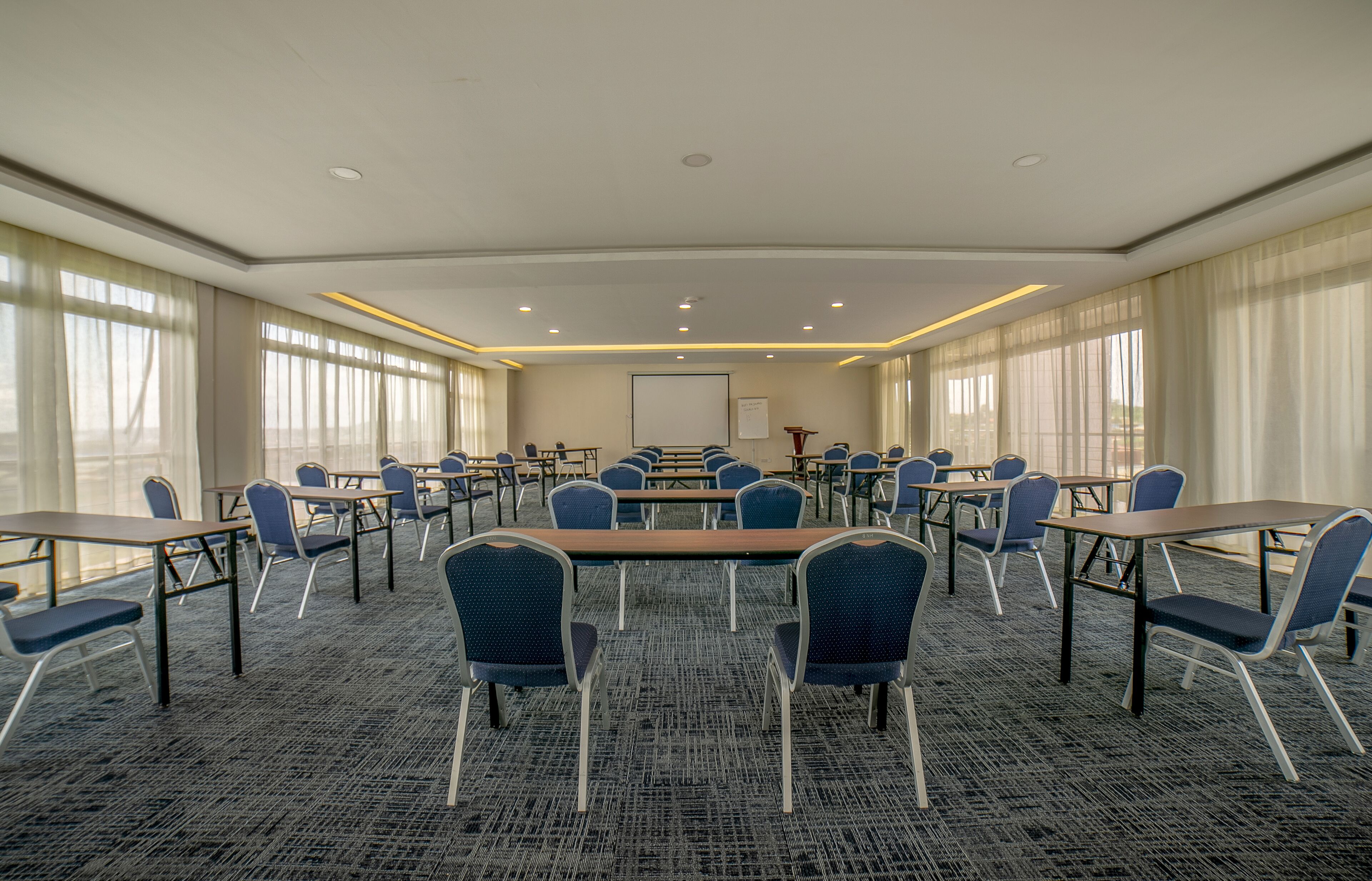 Uma sala de conferências com uma mesa grande, várias cadeiras e uma tela de projeção.