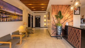 Uma área de recepção de hotel com design moderno, apresentando um balcão de atendimento, espaço de estar e uma grande pintura pendurada na parede de uma ponte.