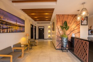 Zona de recepción de hotel con diseño moderno, que incluye un mostrador de recepción, un área de descanso y un cuadro grande colgado en la pared de un puente.