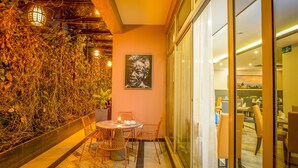 Restaurante com parede de vidro, uma pintura e uma mesa com cadeiras.