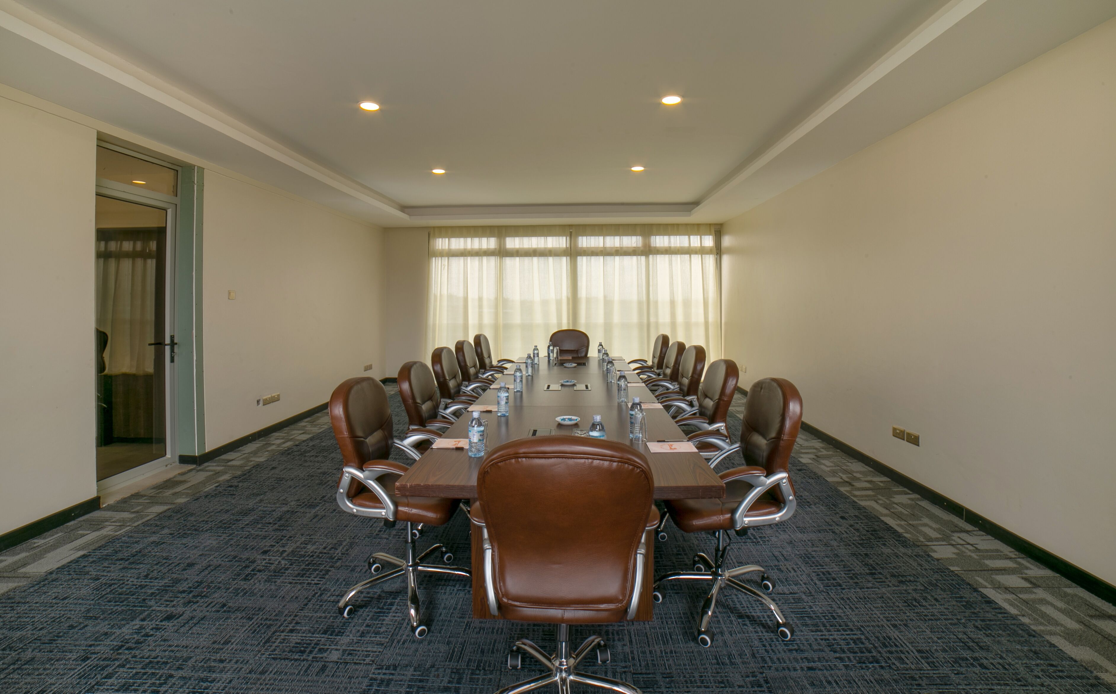 A conference room with a long table, multiple chairs, and a door leading to another room.