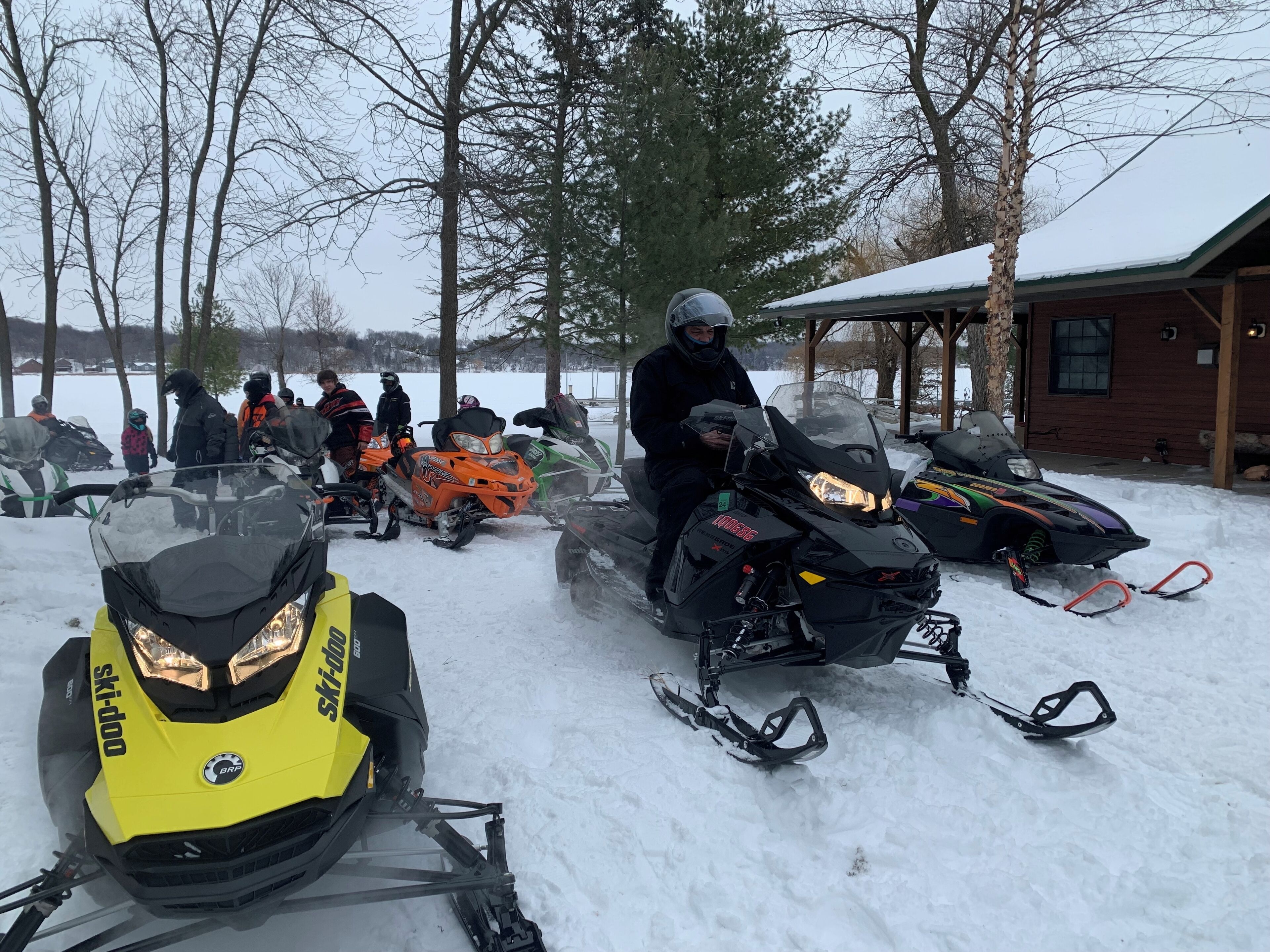 A group of snowmobiles parked in a snowy area with a wooden cabin in the background.