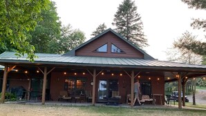 Eine rustikale Lodge mit überdachter Veranda, Sitzgelegenheiten im Freien und einem großen Fenster mit Blick auf die Landschaft.