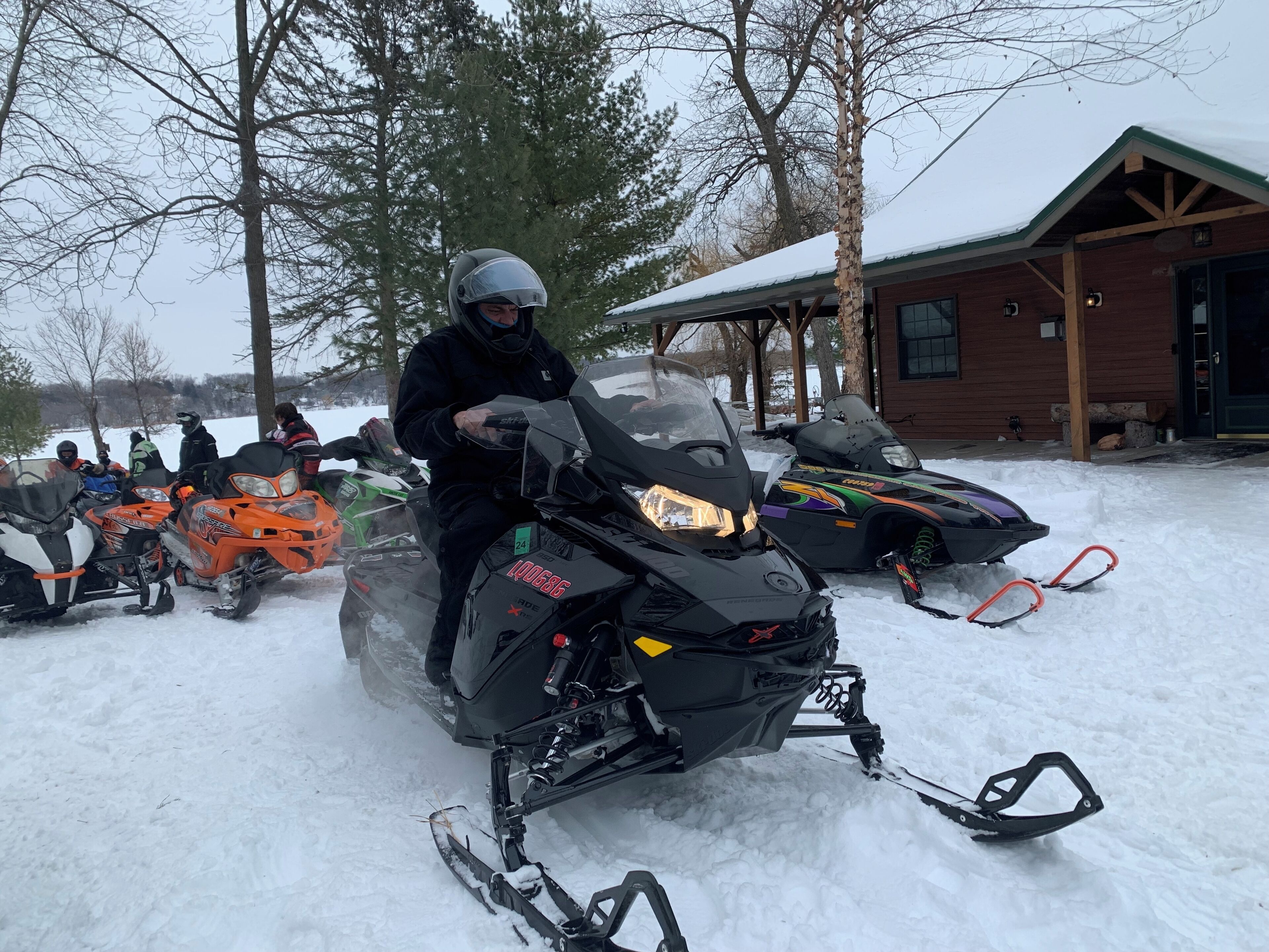 Motos de nieve con placa de identificación y un trineo, estacionadas en una zona nevada con un edificio al fondo.