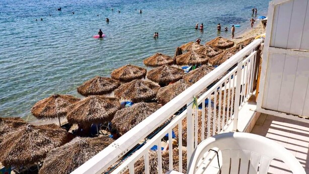 Un balcone con vista sul mare, ombrelloni di paglia e una sedia bianca.