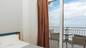 Una camera d'albergo con un letto, un balcone con mobili in vimini e vista sul mare.