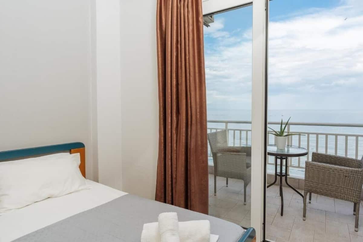 A hotel room with a bed, a balcony with wicker furniture, and a view of the sea.
