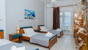 Camera d'albergo con due letti, un quadro raffigurante una costa, un balcone con vista e un vaso con piante essiccate.