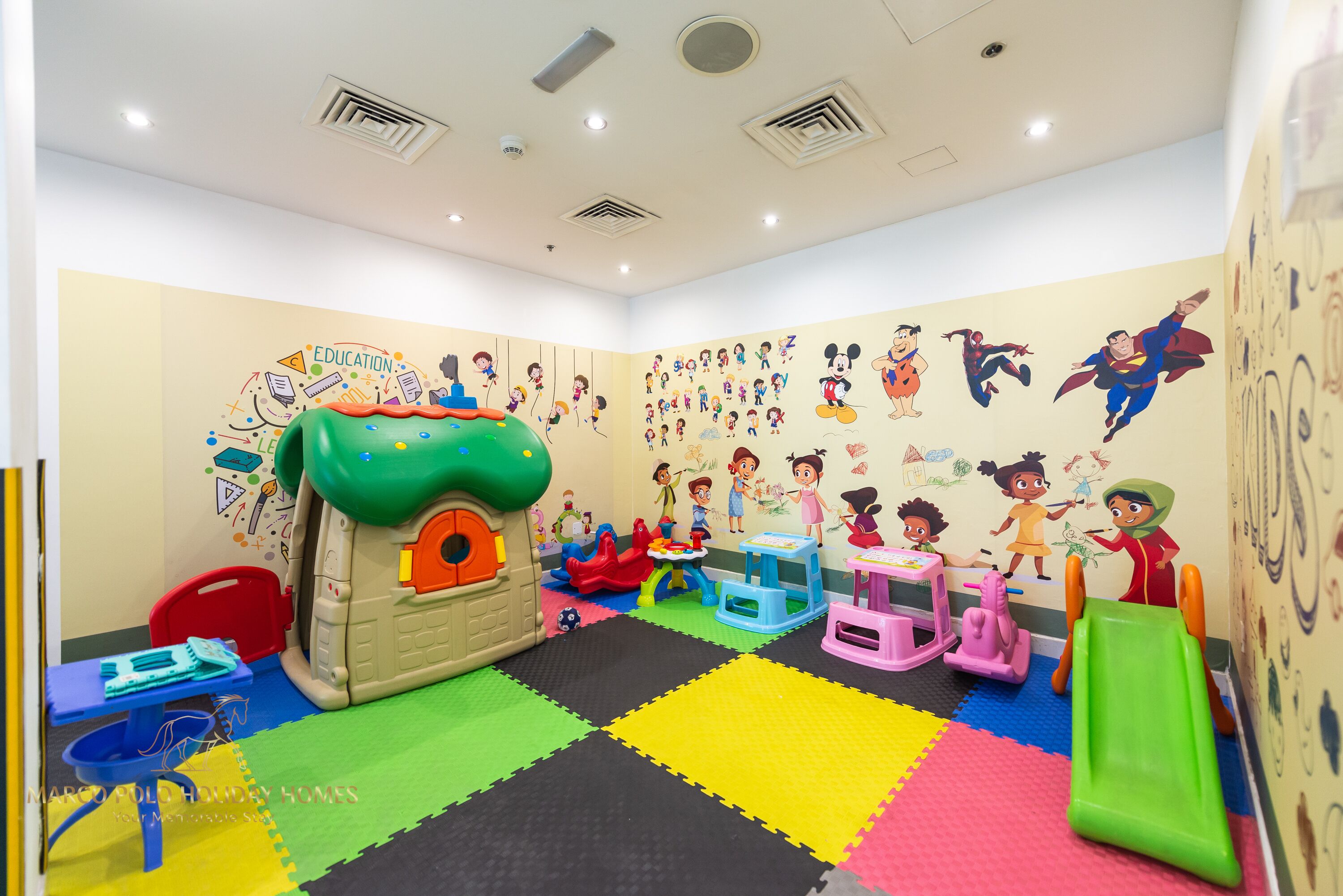 A children's playroom with a playhouse, colorful mats, and educational wall decorations.
