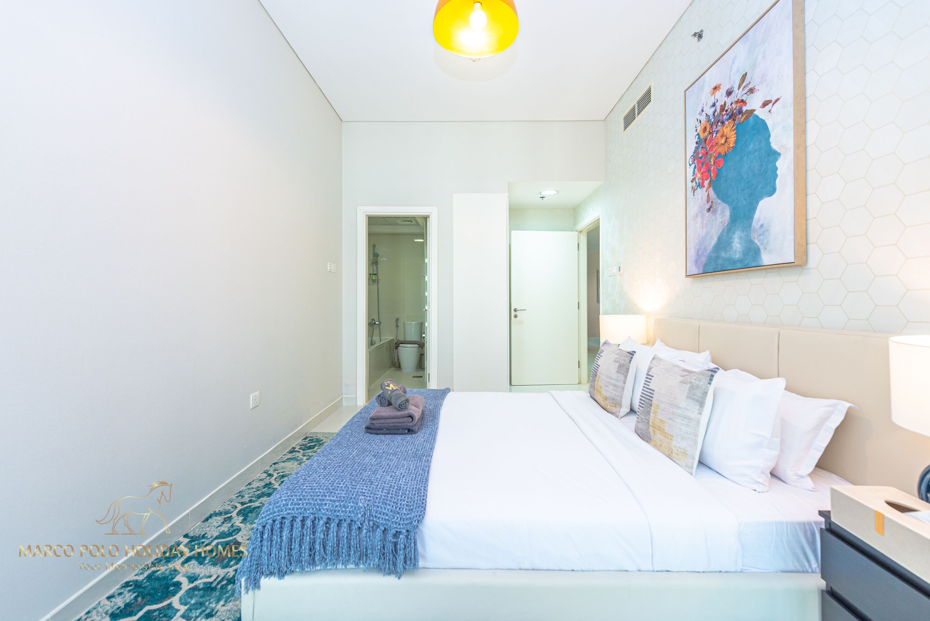 Moderni hotellihuone, jossa on suuri sänky, yöpöytä, seinään kiinnitetty lamppu ja taulu.