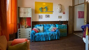 A room with a blue sofa, wooden floor, a yellow light fixture, and a door with a sign.