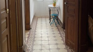 A hallway with patterned floor tiles, a white door with glass panels, and a small table with a plant.