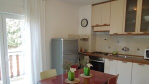 A compact kitchen with a refrigerator, stove, and microwave. There is a dining table with chairs and a vase with flowers. - Apartment in Knin near Knin Fortress (Knin)