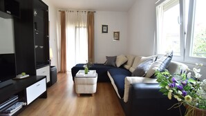 A modern living room with a black sofa, a white ottoman, a flat-screen TV, and a large window with curtains. - Apartment in Knin near Knin Fortress (Knin)