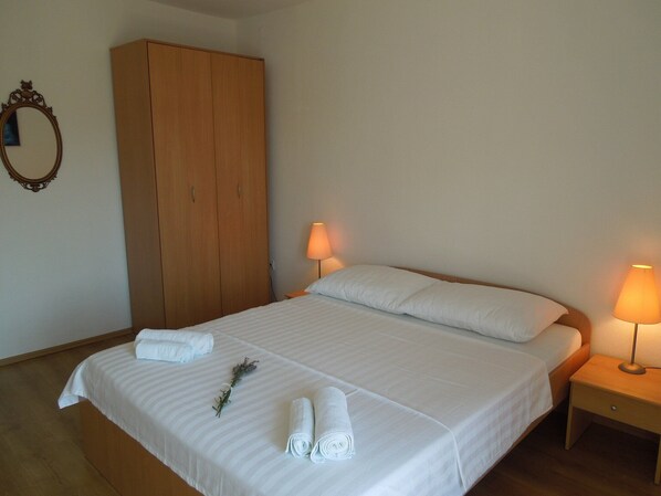A neatly made bed with white linens, two bedside lamps, and a wooden wardrobe.
