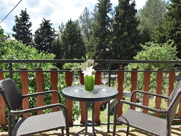 A round table with two wicker chairs, a glass vase with a white flower, and a green vase with a plant.