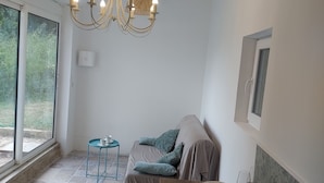 A cozy living area with a sofa, a small table, a chandelier, and a window. - Dépendance D'une Bastide Provençale (MANOSQUE)