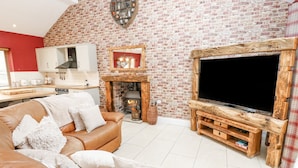A living room with a brick wall, a fireplace, a television on a wooden stand, and a leather sofa.