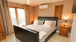 A modern bedroom with a large bed, a bedside table, an air conditioning unit, and a window with blinds.