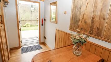 Un interior de madera con una puerta que da al exterior, un banco de madera, una mesa con un florero y un armario de madera.