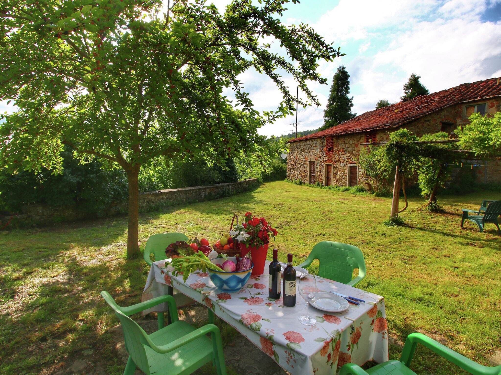 Un área de comedor al aire libre con una mesa dispuesta para dos, rodeada de follaje y un edificio de piedra al fondo.