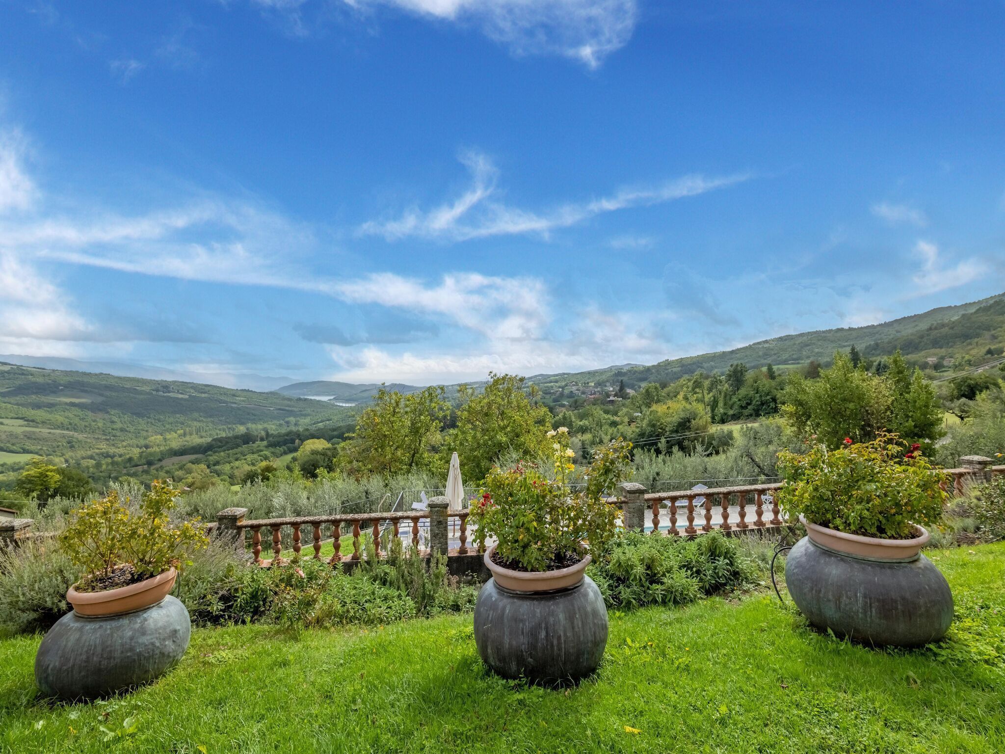 A lush garden with potted plants and a scenic view of rolling hills and a distant lake.