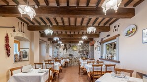 Un restaurant avec des poutres en bois, des murs en pierre et des nappes blanches. Les tables sont dressées avec des verres et des assiettes.