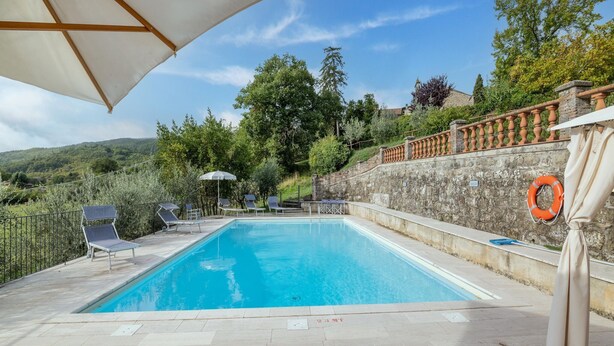 Une piscine entourée de murs de pierre et de verdure, avec des chaises longues et un parasol.