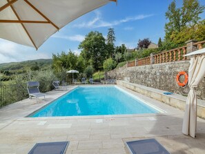 Ein Swimmingpool mit Liegestühlen und einem Sonnenschirm, umgeben von Steinmauern und viel Grün.