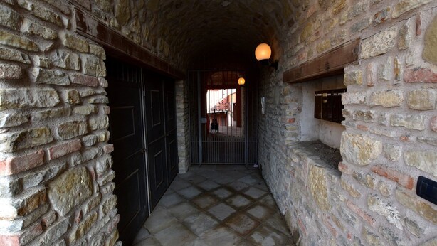 A narrow stone corridor with a tiled floor, stone walls, and a hanging light fixture. - Hillview Langhe Apartment (Belvedere Langhe)