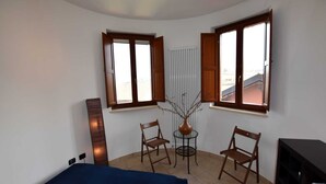 A bedroom with a bed, two chairs, a small table, and a radiator. - Hillview Langhe Apartment (Belvedere Langhe)
