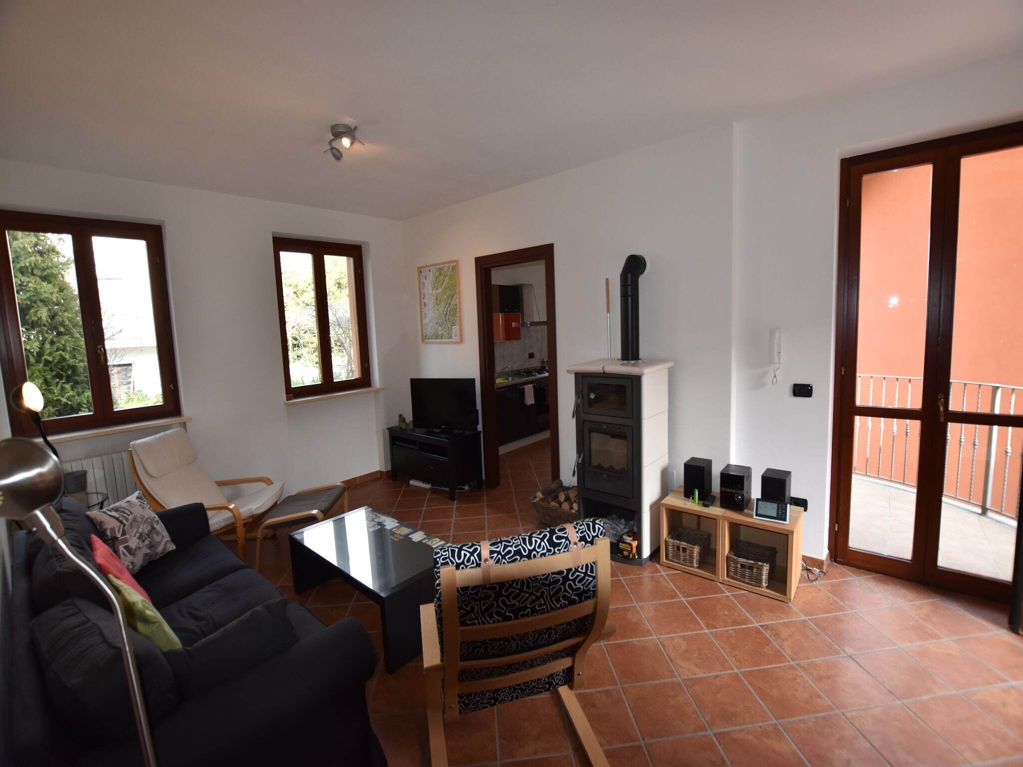 Una sala de estar con un sofá, una mesa de centro y un televisor. Hay una chimenea con un conducto y un balcón visible a través de la puerta.