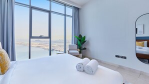 Habitación de hotel con una cama grande, una silla, una planta en maceta y vistas a la ciudad a través de amplios ventanales.