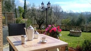 A patio with a table set for tea, surrounded by a garden with a stone fountain and flowering plants. - Apartment in Sabina with Panoramic Views (Selci)