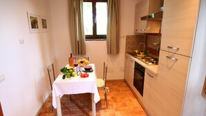 A compact kitchen with a dining table set for two, featuring a white tablecloth, a variety of fruits, and a bottle of wine. - Apartment in Sabina with Panoramic Views (Selci)