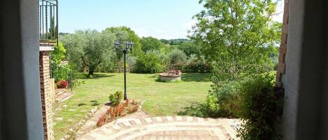 An arched doorway leading to a garden with a brick pathway, a lamp post, and a view of a lush landscape.