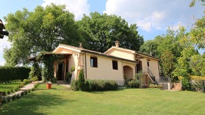 A two-story house with a tiled roof, surrounded by a well-maintained lawn and trees. - Apartment in Sabina with Panoramic Views (Selci)