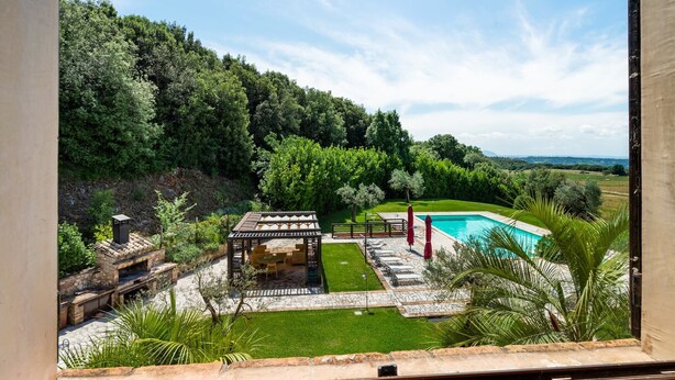 Vue d’un jardin avec une piscine, un espace barbecue et une pergola.