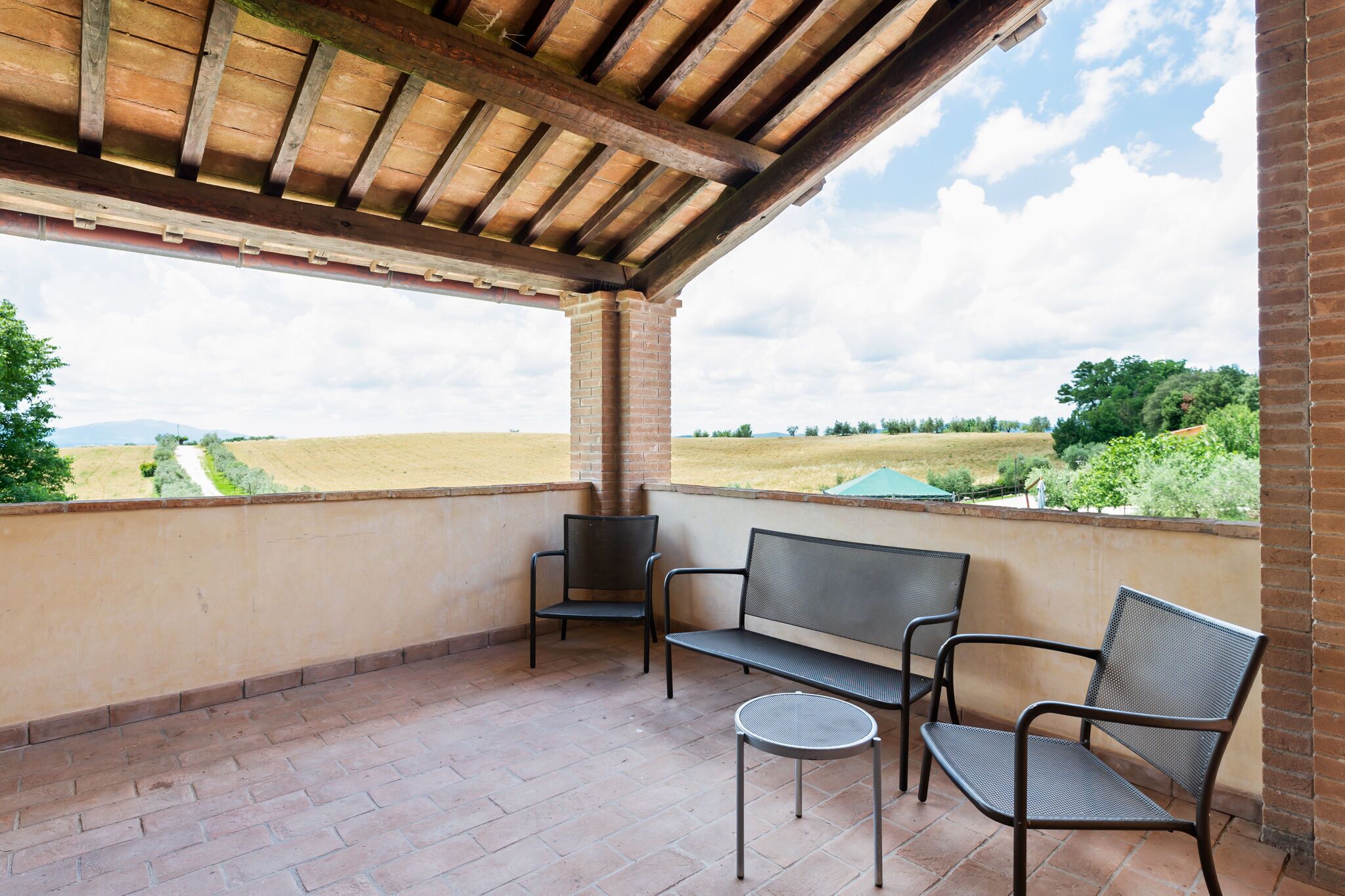 A covered patio with a brick floor, a bench, two chairs, and a small table.